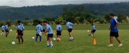 A Projects Abroad volunteer coaching sports in Samoa plays football with a group of children at a local school. Children do football drills during a training session led by a Projects Abroad volunteer sports coach in Samoa.